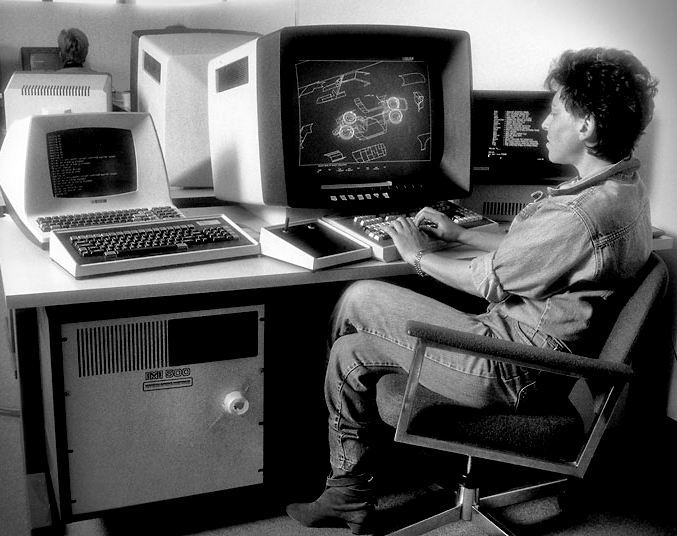 Shelly Lake at Digital Productions 1983. Black and white photograph of a woman wearing in jeans and a denim shirt sitting at a computer terminal. The computer monitor is displaying a vector graphics image.