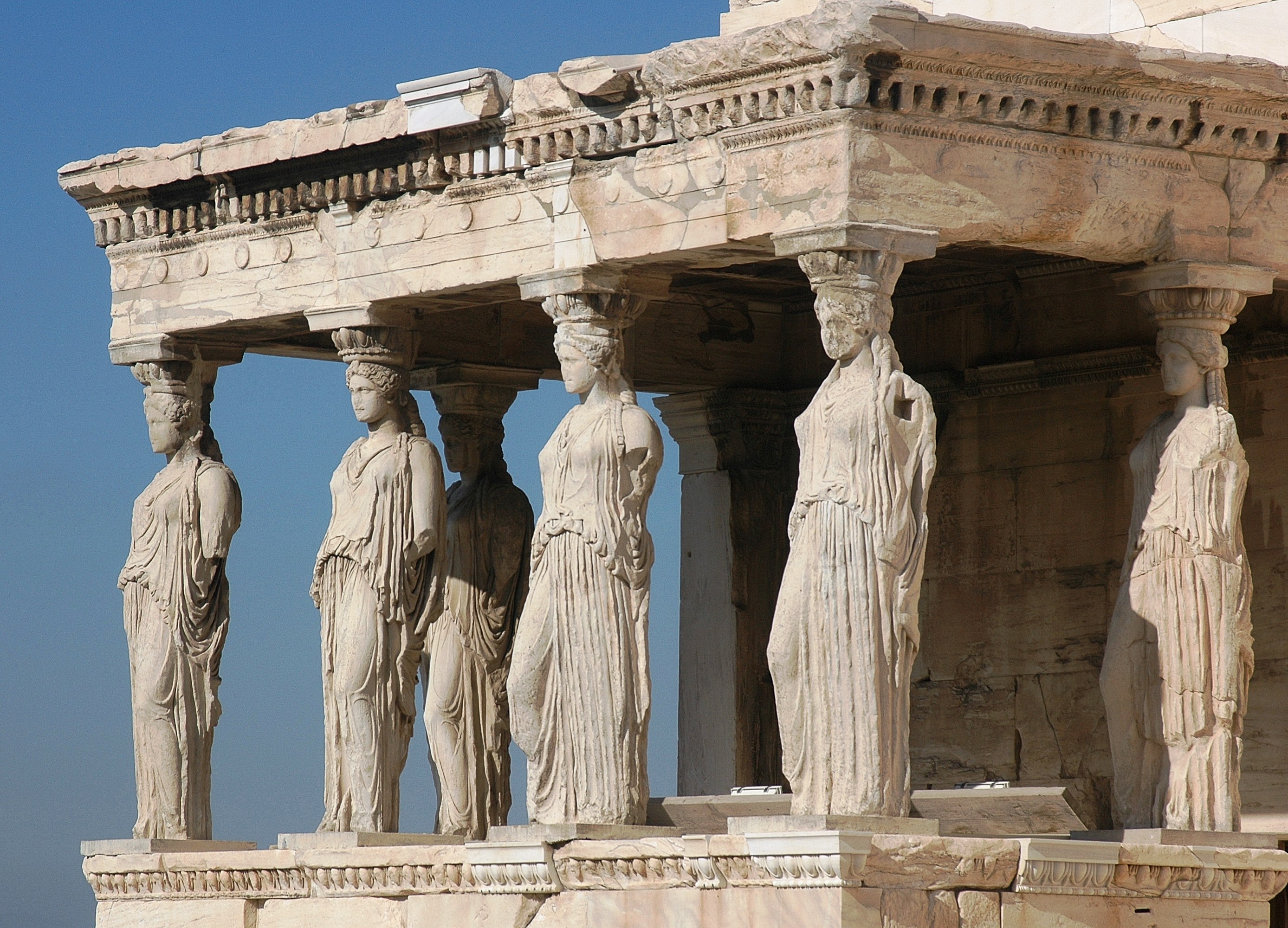 Ancient ruin with 6 sculptures of women wearing heavily draped robes functioning as pillars.